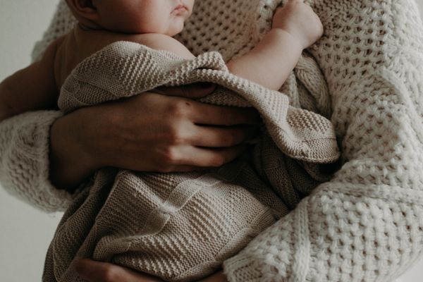 Baby eingewickelt in einem Tuch, in den Armen einer Person, Stillkissen für einen nachhaltigen Start ins Leben